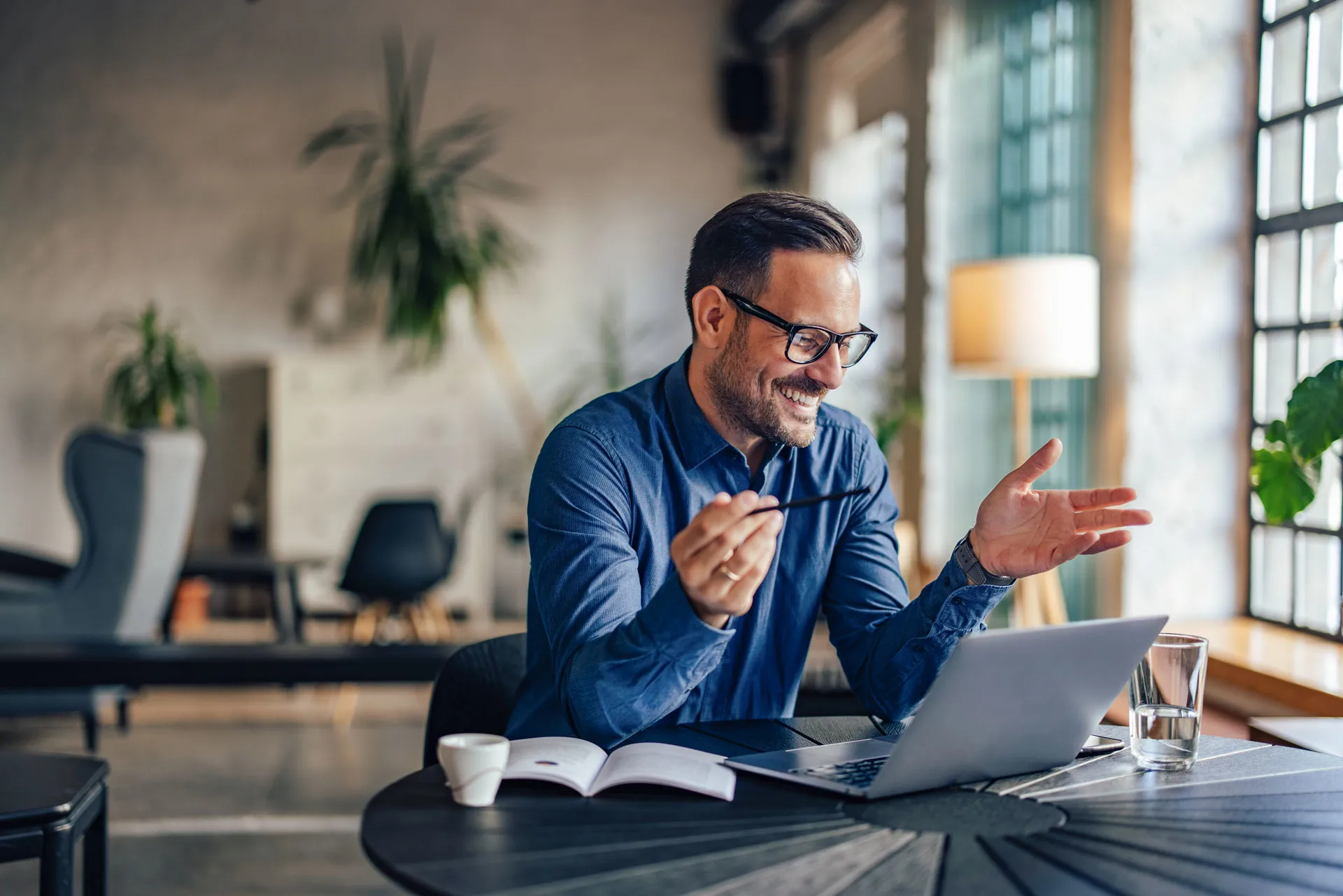 Mann mit blauem Hemd und Brille an einer virtuellen Besprechung vor dem Laptop