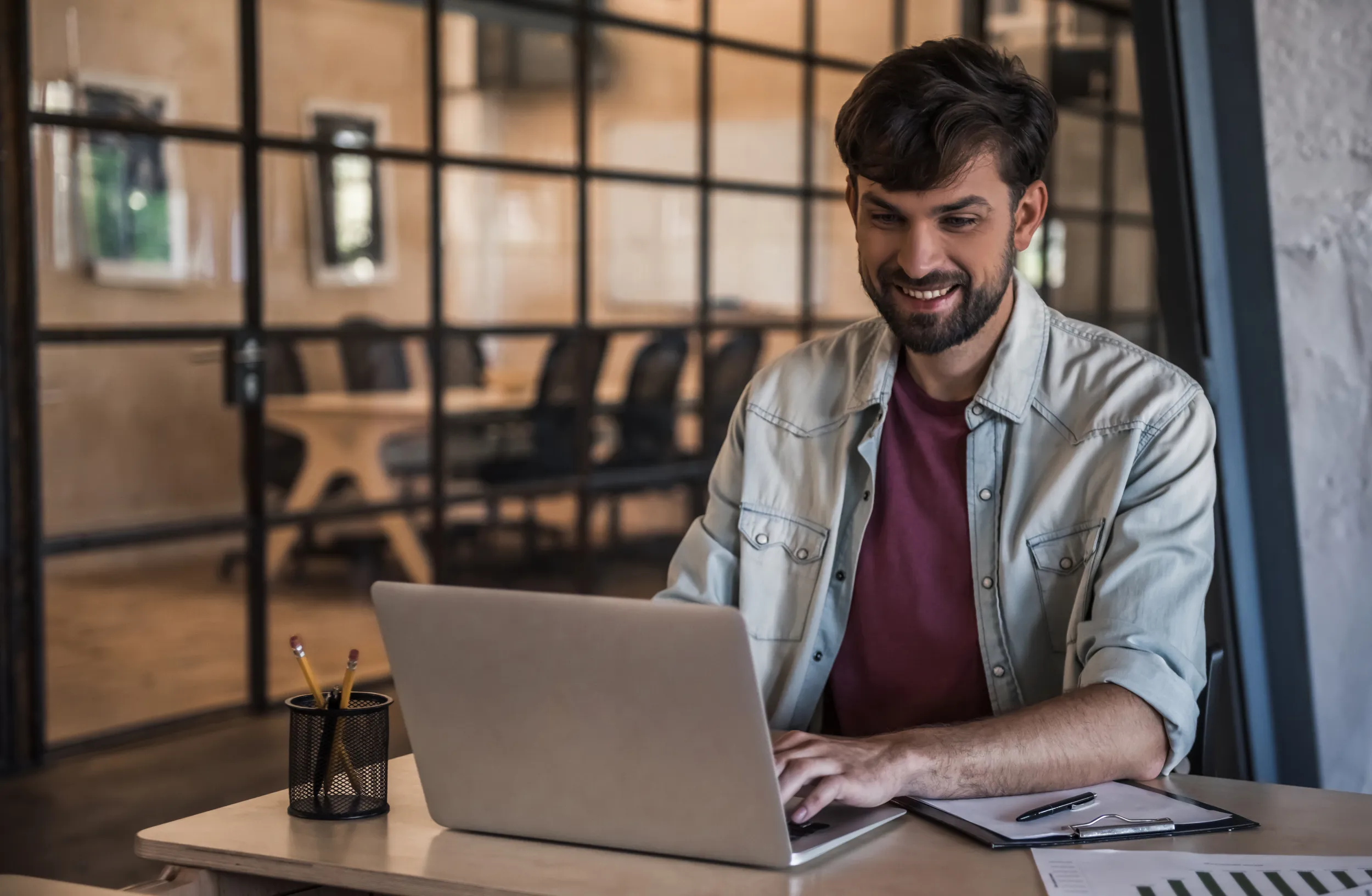 Mann arbeitet an einem Laptop hinter ihm ist ein grosser Besprechungstisch