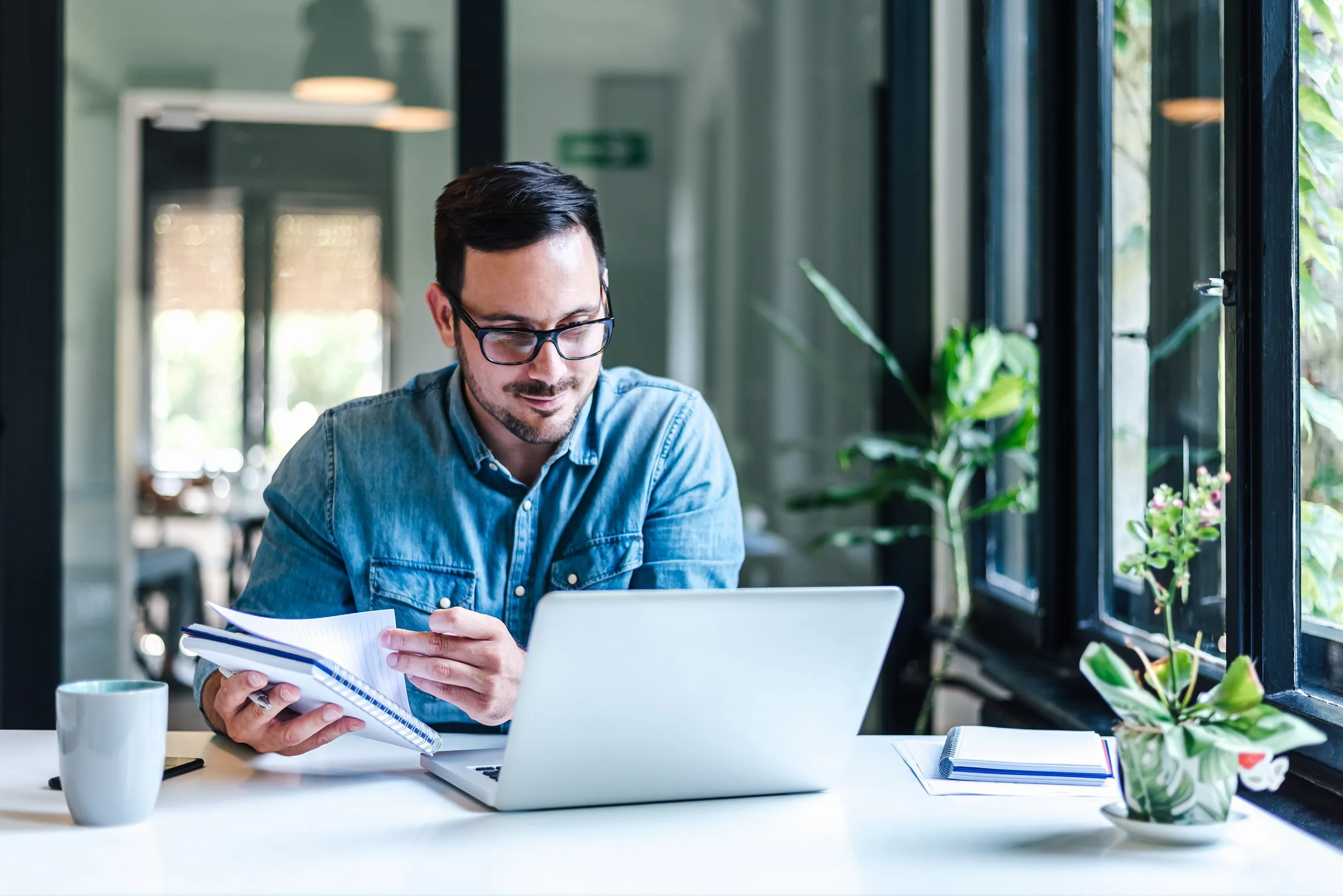 Mann mit Jeanshemd arbeitet lachend in einem Büro mit Pflanzen