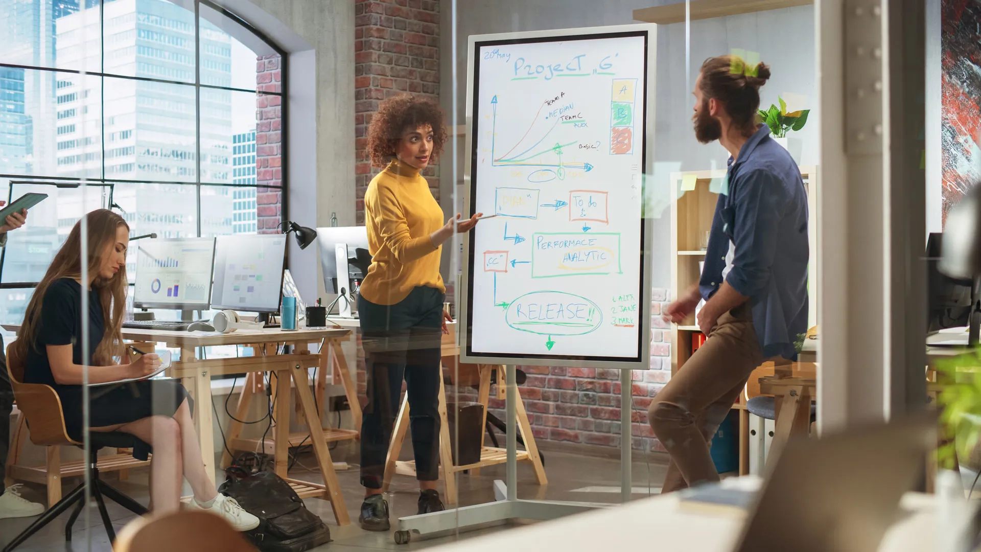 Frau präsentiert ein Projekt auf einem elektronischen Whiteboard vor zwei Personen