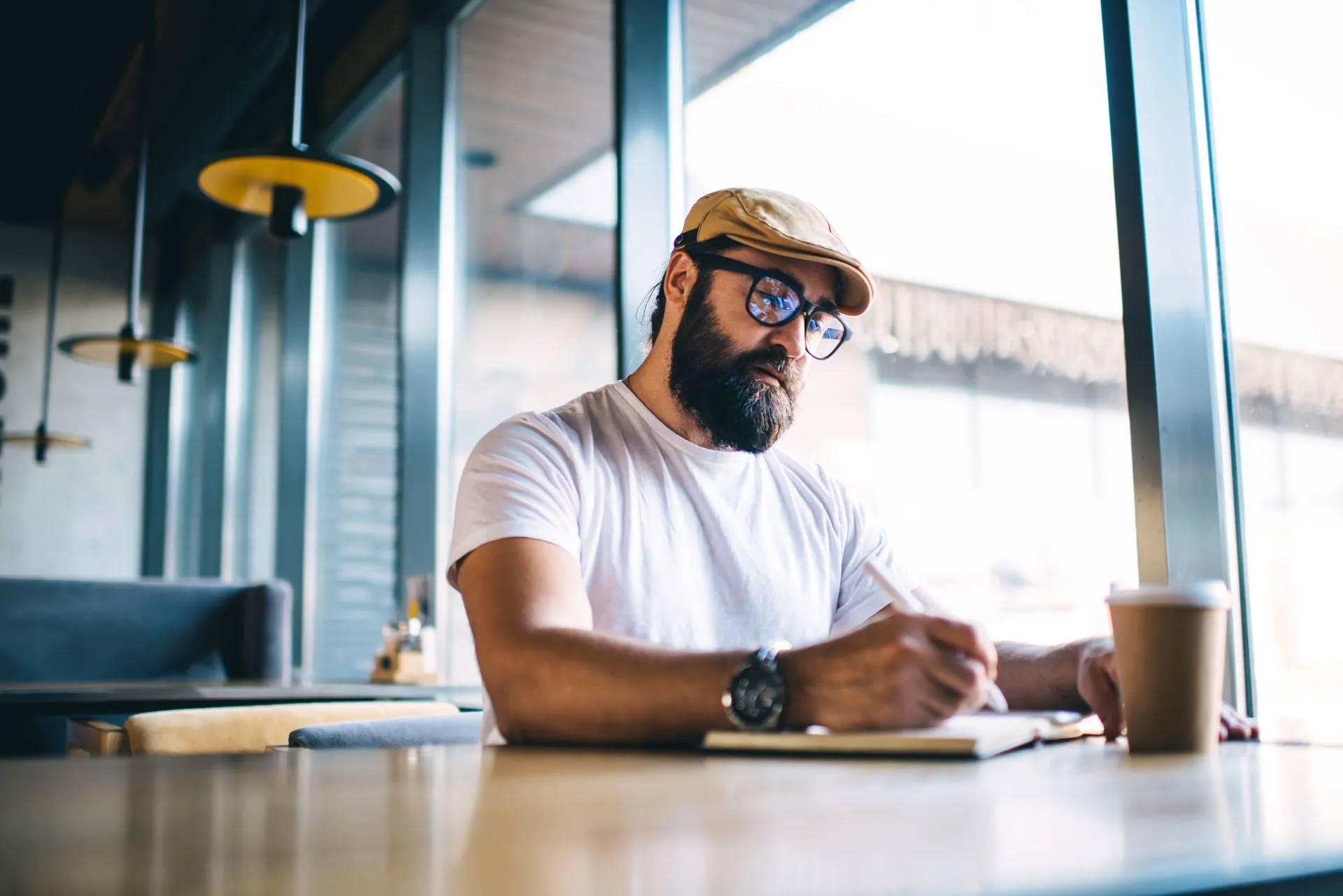 Mann mit Brille sitzt in einem Café und schreibt in sein Notizbuch