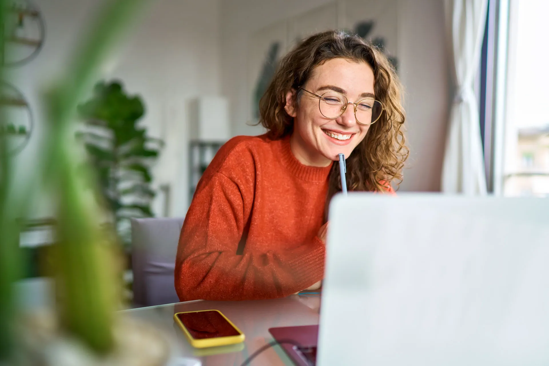 Junge Frau in orangem Pulli lachend und lernend vor dem Laptop