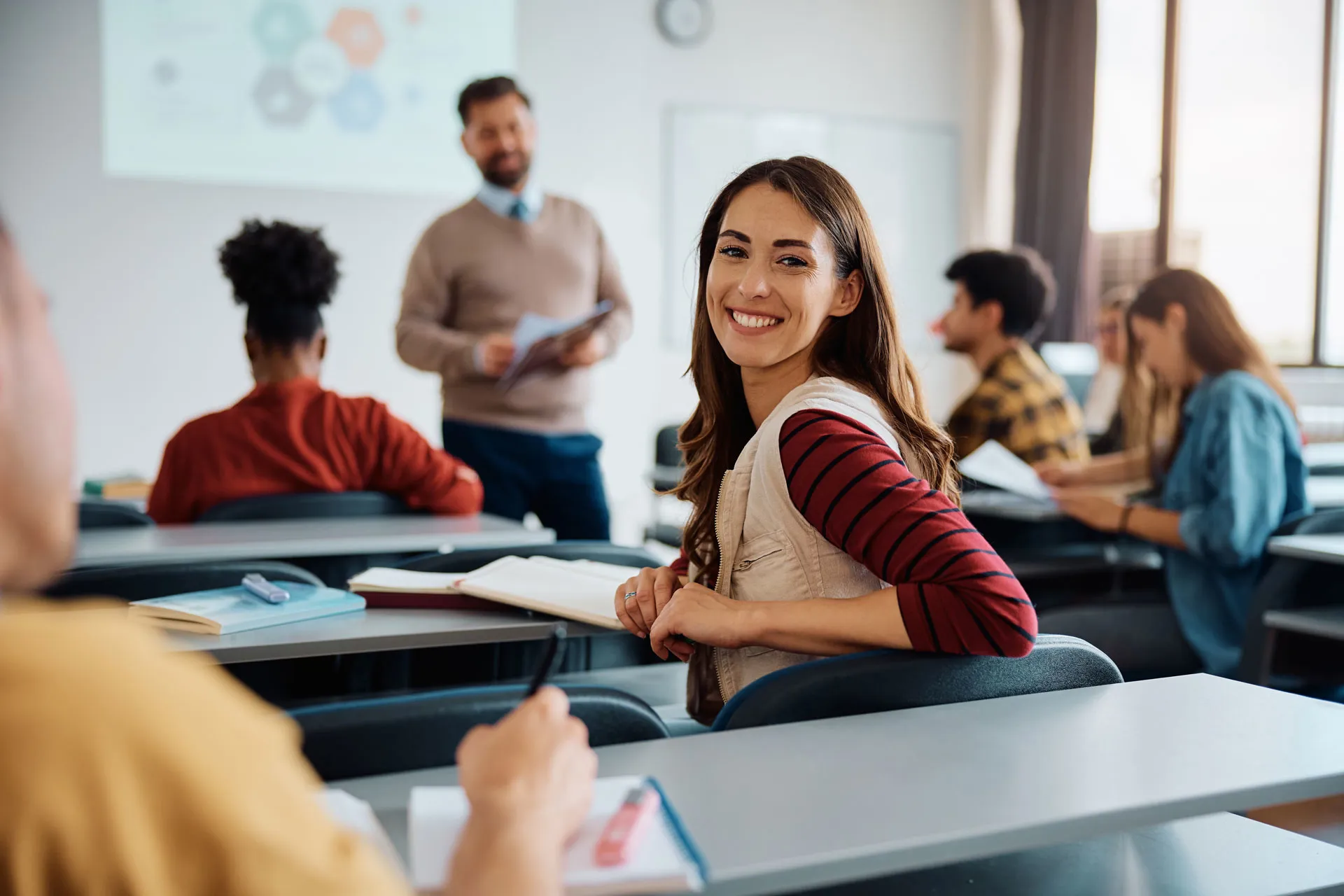 Erwachsene Frau sitzt in einem Klassenzimmer mit anderen Erwachsenen und bekommt Unterricht