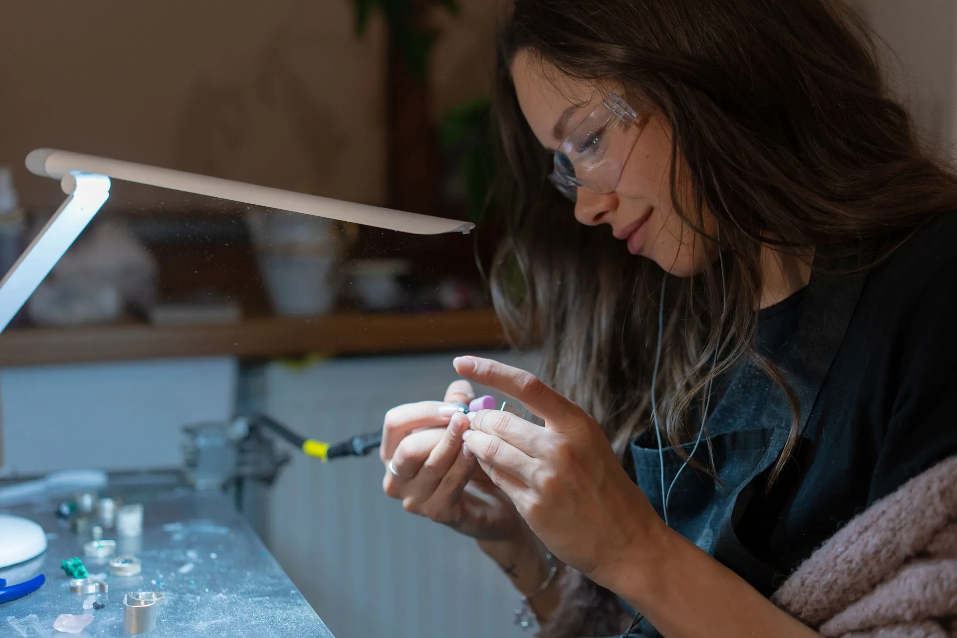 Junge Frau schleift ein Schmuckstück, vor ihr sind verschiedene Werkzeuge und Metalle