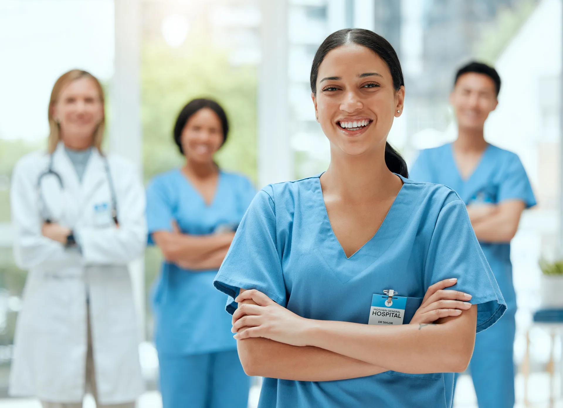 Junge medizinische Praxiskoordinatorin steht im Spital, ihr Team ist im Hintergrund zu sehen